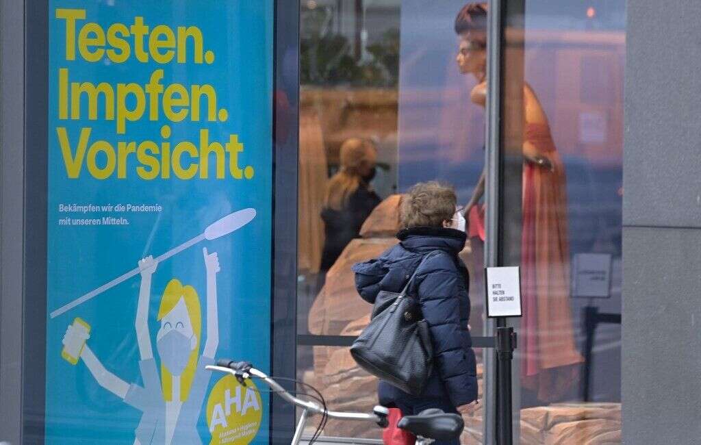 Une femme avec un masque passe devant des boutiques à Berlin, le 29 mars 2021. Sur le panneau à côté figure le slogan; 