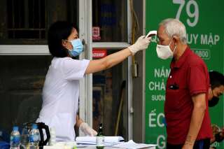 Une professionnelle de santé contrôle la température d'un homme à Hanoi, dimanche 8 mars.
