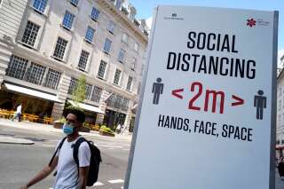 Un passant portant un masque devant un panneau demandant aux personnes de respecter les mesures de distanciation à Londres le 7 juin.