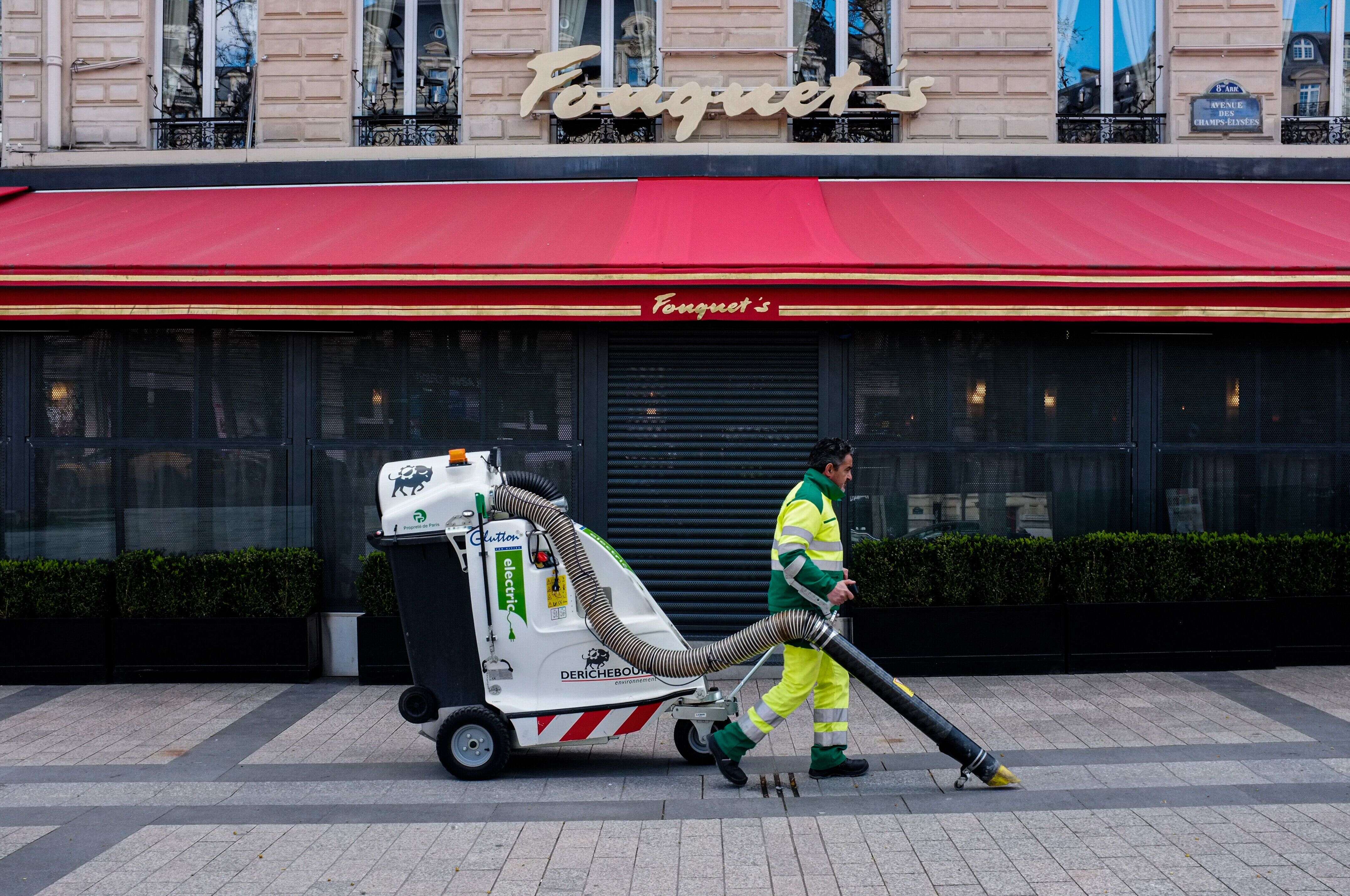 Un employé chargé de la propreté nettoie la rue devant le Fouquet's sur les Champs-Elysées à Paris, au lendemain de l'annonce par Édouard Philippe de la fermeture des restaurants afin de lutter contre l'épidémie de coronavirus, le 15 mars 2020.