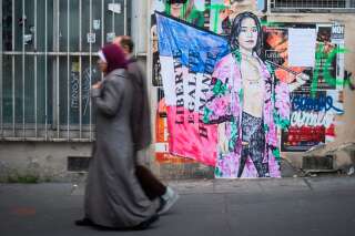Une photo prise à Paris le 2 mai 2017 avant le second tour de l'élection présidentielle française montre un couple dont la femme est voilée passant devant l'illustration d'une femme partiellement dénudée et qui brandit le slogan 