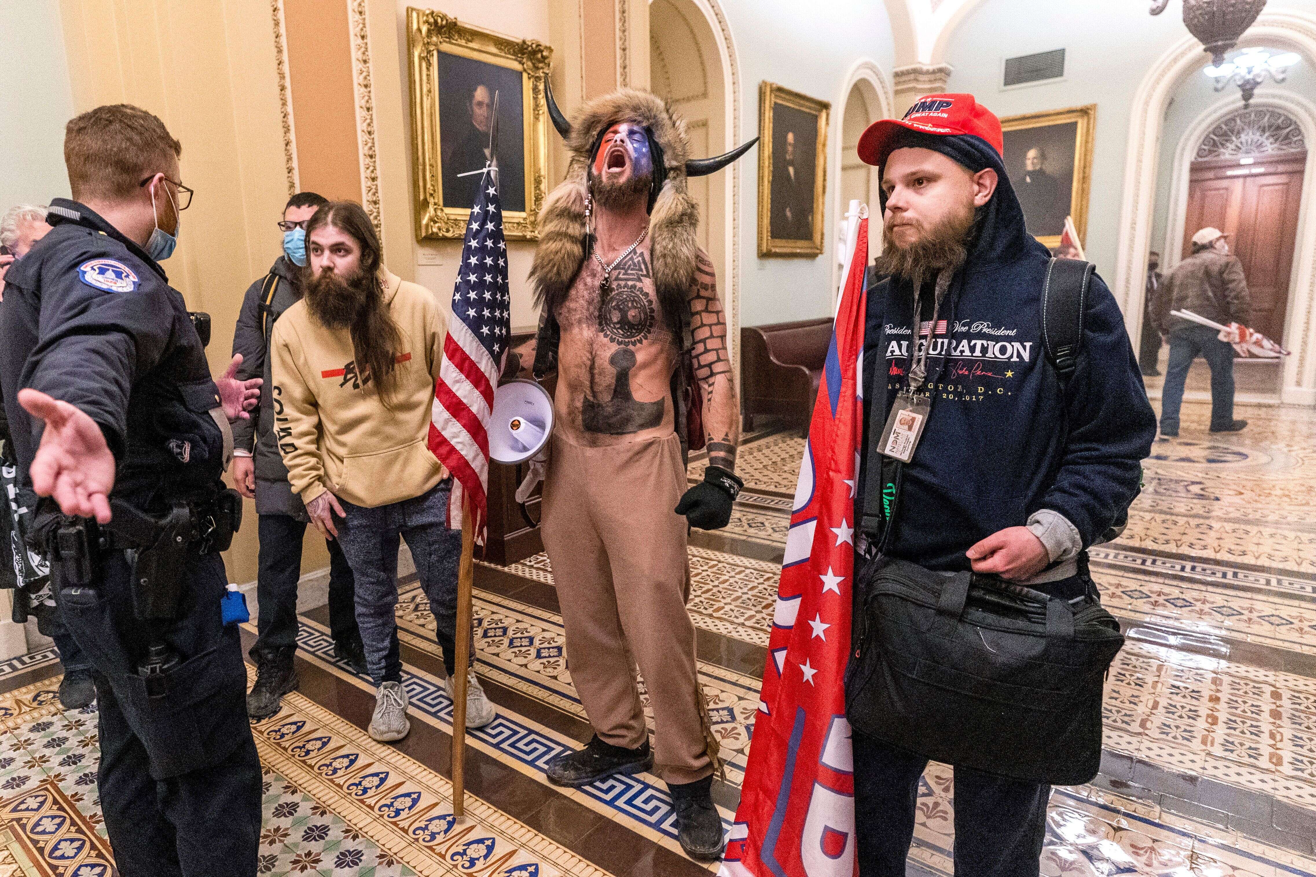 Jacob Chansley, entouré de soutiens de Donald Trump, fait face à des policiers du Capitole devant l'enceinte du Sénat le 6 janvier 2021.