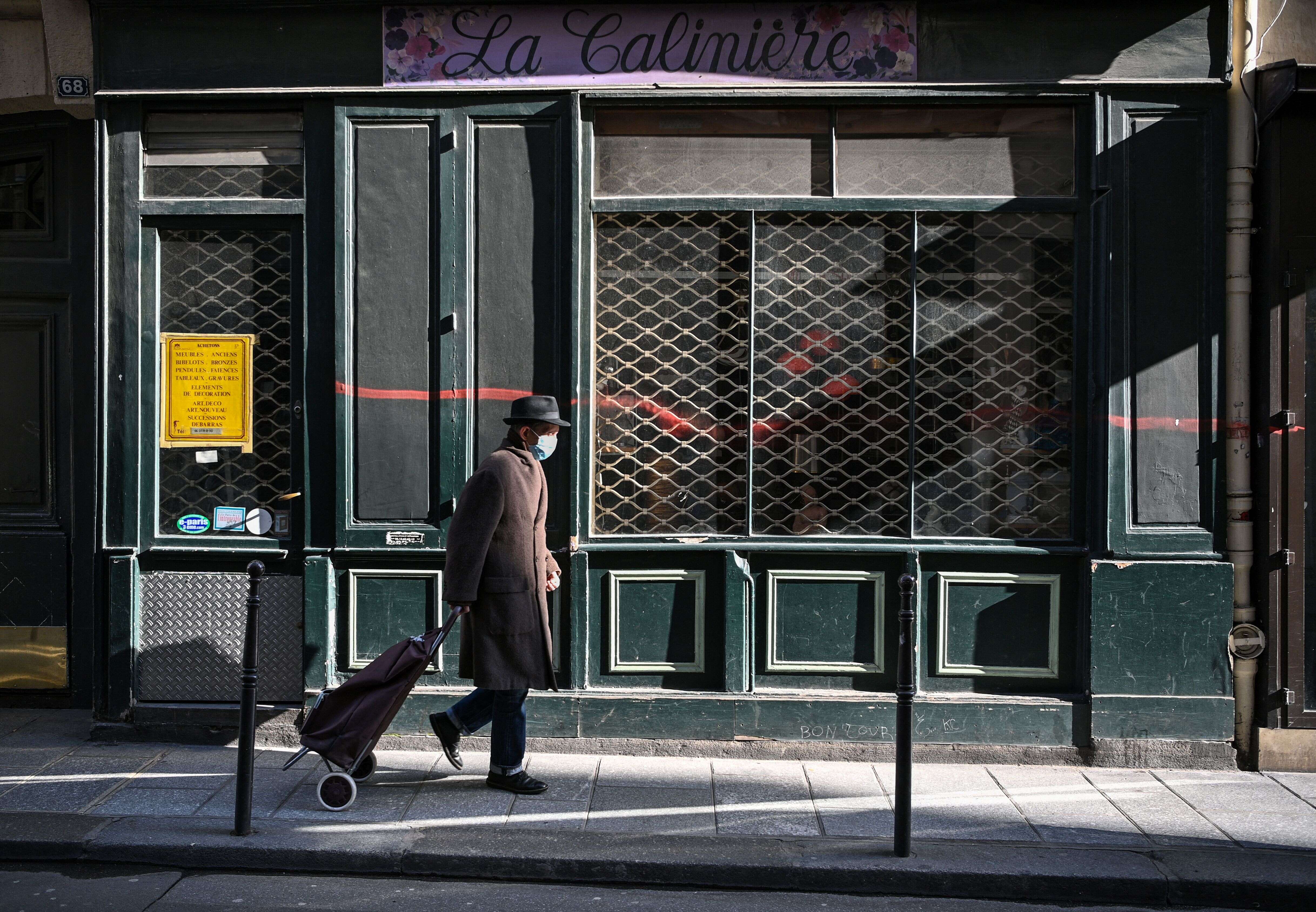 Un homme marche devant la devanture d'un magasin fermé à Paris le 20 mars 2021.