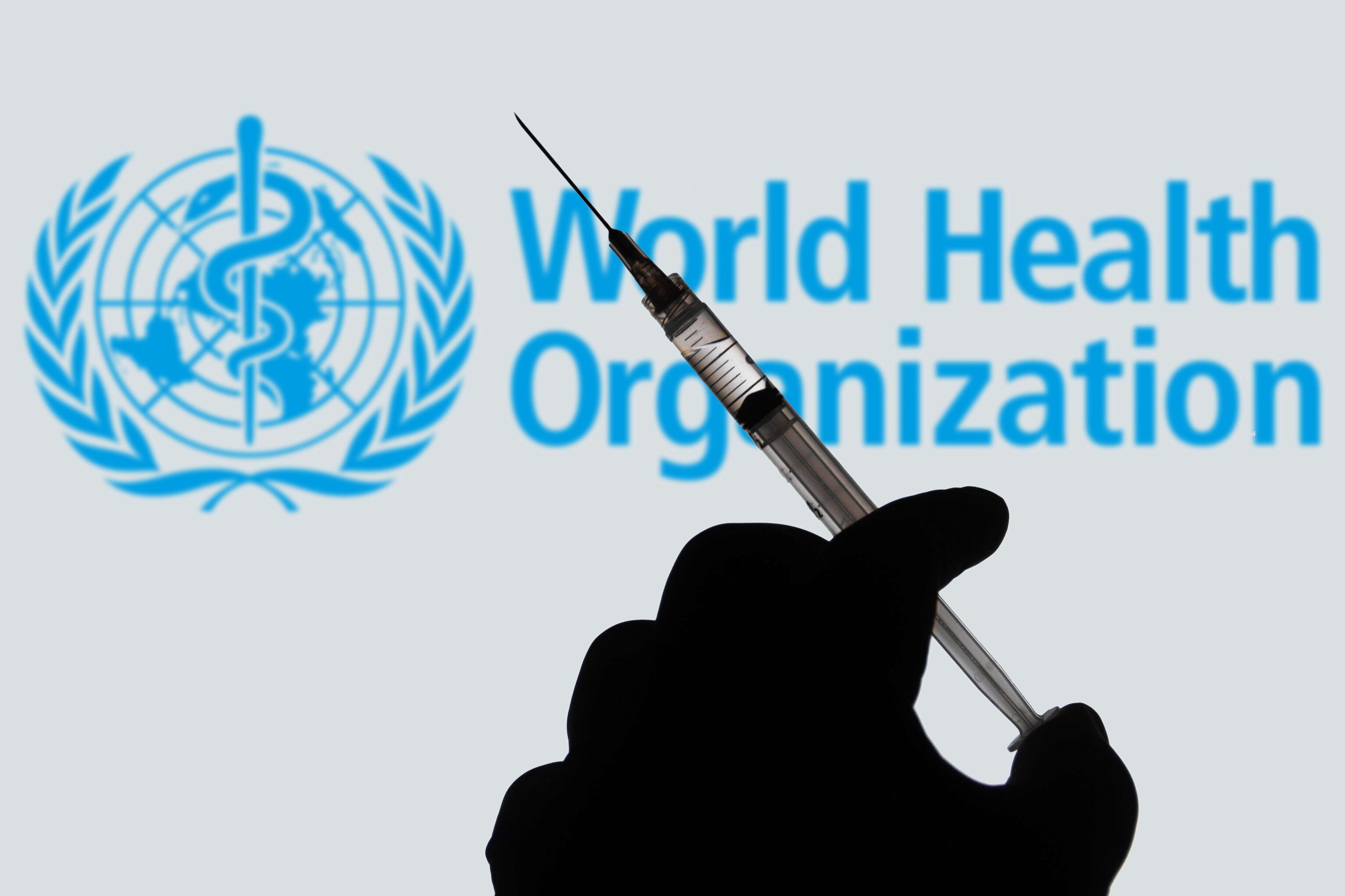 BRAZIL - 2021/04/02: In this photo illustration, a hand holds a medical syringe with a World Health Organization (WHO) company logo displayed on a screen in the background. (Photo Illustration by Rafael Henrique/SOPA Images/LightRocket via Getty Images)