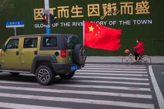 Un véhicule portant le drapeau chinois passe à côté d'une femme portant un masque alors qu'elle est à vélo dans la ville de Wuhan, dans la province de Hubei, en Chine, le mercredi 29 janvier 2020. (AP Photo/Arek Rataj)