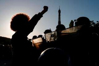 Des manifestants lèvent le poing devant les policiers anti-émeutes lors d'une manifestation au Champ de Mars, à Paris le 6 juin 2020, dans le cadre des manifestations mondiales 