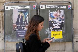 A woman walks in front of torn campaign posters of French President Emmanuel Macron and candidate for the reelection, right, and of far-right presidential candidate Marine Le Pen, left, in Paris, France, Tuesday, April 19, 2022. French President Emmanuel Macron is facing off against far-right challenger Marine Le Pen in France's April 24 presidential runoff. (AP Photo/Francois Mori)