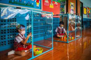 L'école Wat Khlong Toey à Bangkok, en Thaïlande, a mis en place un protocole sanitaire très strict depuis sa réouverture début juillet. Les enfants jouent séparément, chacun dans un cube de plastique ou de plexiglas.