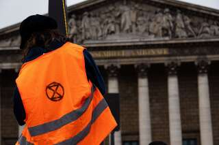 Un militant portant un gilet orange avec le logo du mouvement écologiste Extinction Rebellion s'est hissé sur un poteau devant l'Assemblée nationale lors de la semaine d'action 