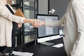 Midsection of businesswoman shaking hands with pregnant coworker in modern office