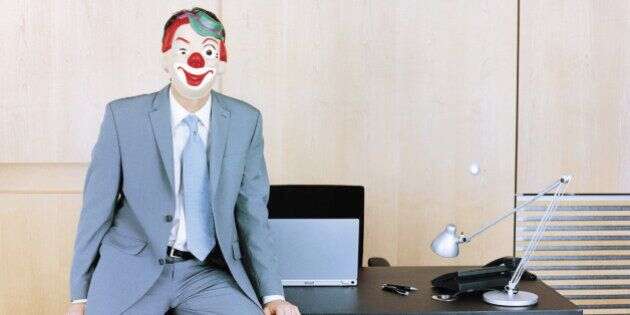Businessman sitting at edge of desk wearing clown mask