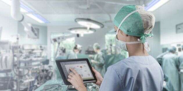 Female surgeon using digital tablet to command artificial heart in operation room.
