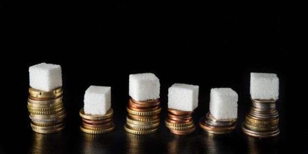 Piles of coins with sugar cubes and bottles filled with sugar on top, symbolising sugar tax, on black slate background