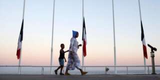 A woman and her child pass by French flags at half mast near the site of a deadly attack on the famed Boulevard des Anglais in Nice southern France, Saturday, July 16, 2016. French Interior Minister Bernard Cazeneuve says that the truck driver who killed 84 people when he careened into a crowd at a fireworks show was