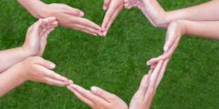 Many arms and hands of girls making heart shape above green grass. Several teens hands joining in figure isolated on green grass background. Five teenagers have bare arms stretched with hands close to each other. Concept of team, teamwork, together, group, unite, binding, bond, agreement, trust, combine, connection, contact, friends, friendship, girlfriends, play, fun, enjoy, partners, colleagues, support, motivate, love, loving, help, helping, piece