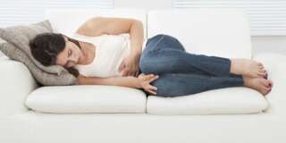 High angle view of young woman suffering from stomachache on sofa at home