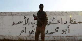 Un soldat syrien devant un mur de graffitis où il est écrit
