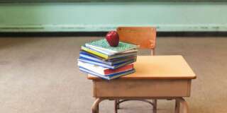 Stack of school books and apple on desk in empty classroom