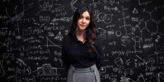 A young woman stands serious in front of a chalkboard filled with mathematical equations, showing individuality, intelligence and creativity