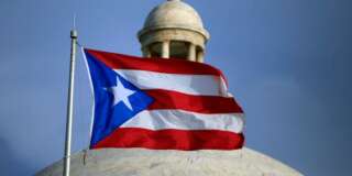 In this Wednesday, July 29, 2015 photo, the Puerto Rican flag flies in front of Puerto Ricoâs Capitol as in San Juan, Puerto Rico. Nearly 10 years into a deep economic slump, Puerto Rico is no closer to pulling out, and, in fact, is poised to plummet further. The unemployment rate is above 12 percent and tens of thousands have migrated out of the island. (AP Photo/Ricardo Arduengo)