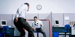 Two businessmen playing soccer in office, goalie catching ball