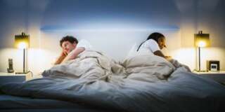 Multi-ethnic couple ignoring each other while lying in bed at home