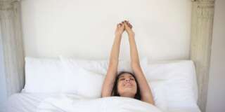 Woman stretching and waking up in bed at home
