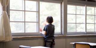 Boy (6-7) looking out of classroom window, rear view