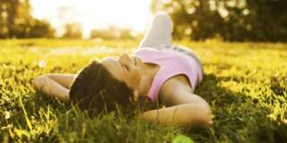 Teenage girl lying on grass with her eyes closed and enjoying the sunset.