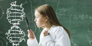 girl in a classroom standing in front of a chalkboard looking at a double helix model with a magnify