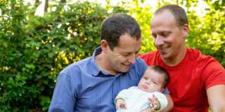 Caucasian gay couple smiling with baby boy in backyard