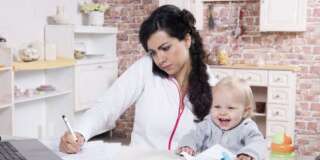 Mother with baby in the kitchen working with documents and speaks by phone