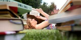 young woman lying on grass in garden reading books