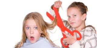 Two teenage girls cutting hair with big red scissors.