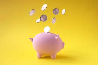 Coins falling into pink piggy bank on yellow background.