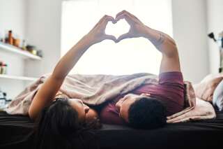 Shot of a happy young couple making a heart shaped gesture with their hands in bed at home