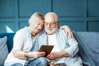 Lovely senior couple dressed casually using digital tablet while sitting together on the comfortable couch at home