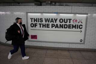 L'Angleterre abandonne le port du masque en intérieur dans les lieux publics (Photo prise dans le métro londonien d'une personne masquée marchant devant un panneau publicitaire 'sortie de la pandémie', le 20 janvier 2022. AP Photo/Kirsty Wigglesworth)