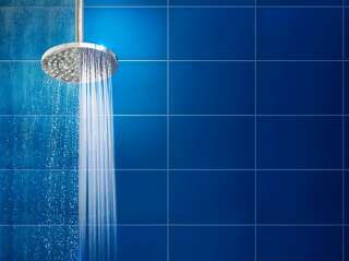 Water streaming from shower head against clean and limescale tile