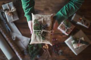 Close up stock photo with unrecognizable female hands holding gift wrapped with textile and natural decoration.