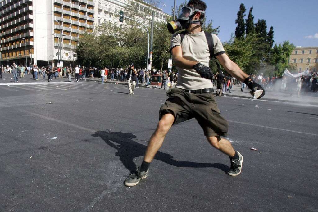 Greece Crippled By General Strike - ATHENS, GREECE - OCTOBER 18:  Protesters throw stones at riot police officers during a 24-hour nationwide general strike on October 18, 2012 in Athens, Greece. Hundreds of youths pelted riot police with petrol bombs, bottles and chunks of marble today as yet another Greek anti-austerity demonstration descended into violence.  (Photo Milos Bicanski/Getty Images)
