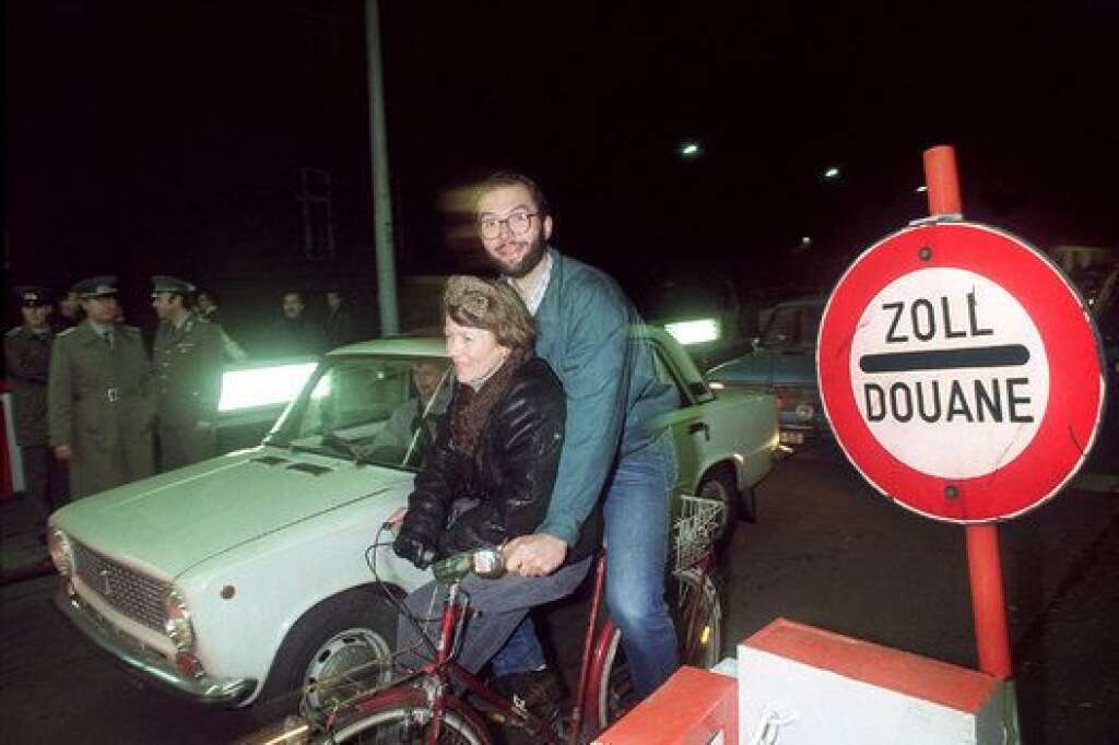 Nuit du 9 au 10 novembre 1989 - Un couple traverse à bicyclette l'un des principaux postes de frontières du mur, alors que les voitures font la queue pour rejoindre l'Allemagne de l'Ouest.