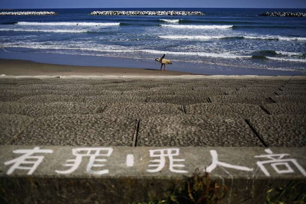 - Un surfeur attend sa vague par delà une barrière anti-tsunami (en premier plan).