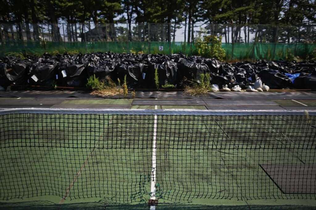 - De gros sacs plastiques contenant de la terre, des feuilles et des débris contaminés sont entreposés sur un court de tennis.