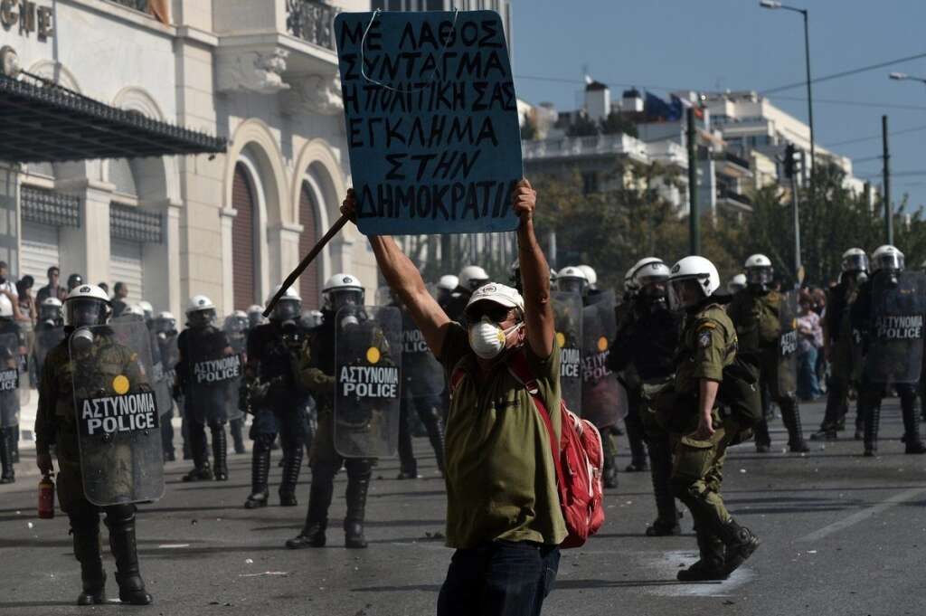 GREECE-FINANCE-PUBLIC-DEBT-EU-STRIKE - A protester holds a placard  in front of riot police forces during a rally marking a 24-hour general strike on October 18, 2012 near the parliament in Athens. Greek riot police on Thursday fired tear gas to disperse protesters at an anti-austerity rally in Athens held during a national general strike as EU leaders were to tackle the eurozone crisis at a summit in Brussels.  AFP PHOTO / ARIS MESSINIS        (Photo credit should read ARIS MESSINIS/AFP/Getty Images)