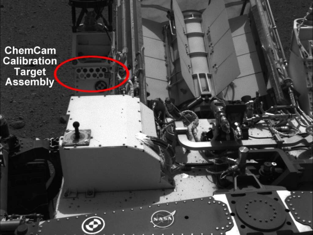 Readying ChemCam - This image shows the calibration target for the Chemistry and Camera (ChemCam) instrument on NASA's Curiosity rover. The calibration target is one square and a group of nine circles that look dark in the black-and-white image. The calibration target set can be seen in the middle left in this image, to the right of the rover's power source. The materials used in these circles are the types of materials scientists anticipated they might encounter on Mars. The square is a titanium alloy with a painted edge.     The ChemCam instrument will be firing a series of powerful, but invisible, laser pulses at a target rock or soil. It is located on the rover's mast, near the Navigation camera that took this image. A telescopic camera known as the remote micro-imager will show the context of the spots hit with the laser.     This image was taken by the right-side Navigation camera on Aug. 16, 2012. (NASA)