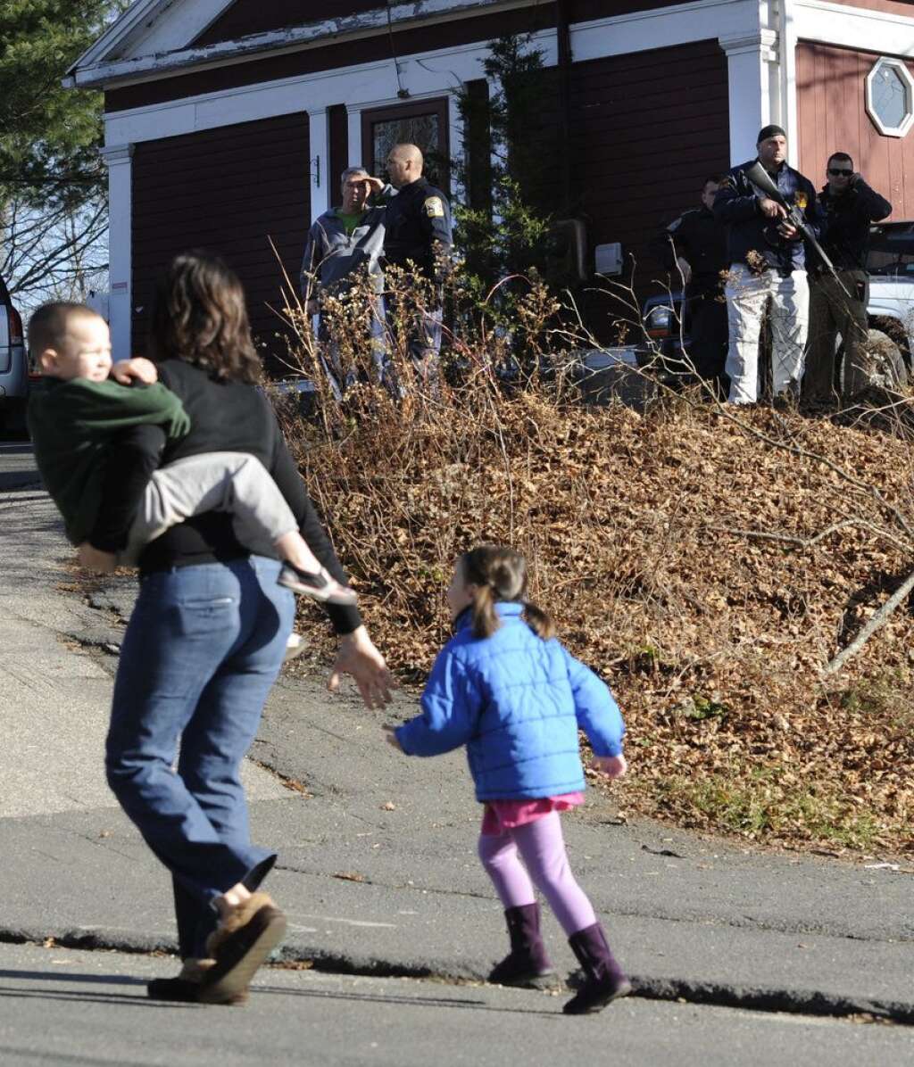 Sandy Hook Elementary School Shooting - A mother runs with her children as police above canvass homes in the area following a shooting at the Sandy Hook Elementary School in Newtown, Conn. where authorities say a gunman opened fire, leaving 26 people dead, including 20 children, Friday, Dec. 14, 2012. (AP Photo/Jessica Hill)