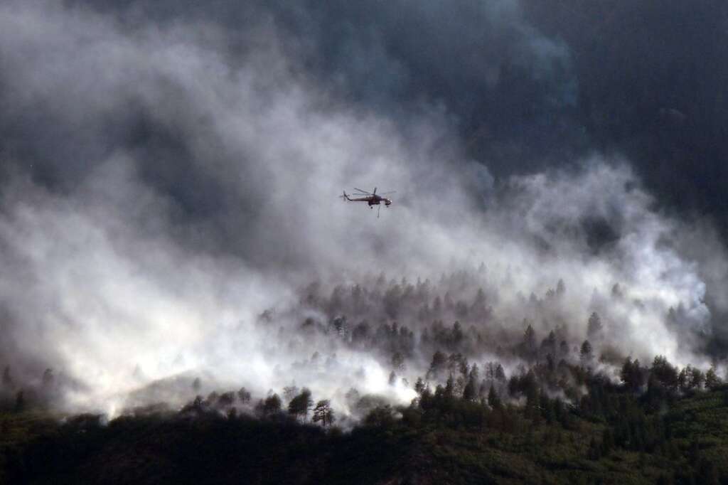 A helicopters flies over as the Waldo Canyon Fire continues to burn Wednesday, June 27, 2012, in Colorado Springs, Colo. The wildfire doubled in size overnight to about 24 square miles (62 square kilometers), and has so far forced mandatory evacuations for more than 32,000 residents. (AP Photo/Bryan Oller)