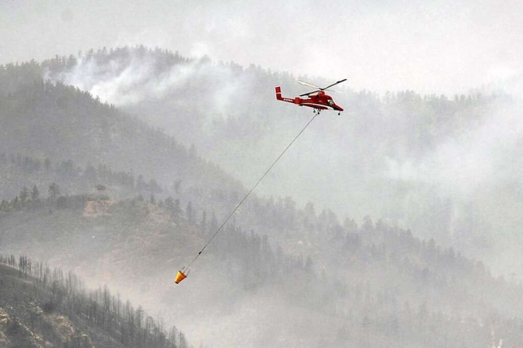 A helicopter flies past the charred mountainside above Queens Canyon as the Waldo Canyon Fire burns Wednesday, June 27, 2012, in Colorado Springs, Colo. The wildfire doubled in size overnight to about 24 square miles (62 square kilometers), and has so far forced mandatory evacuations for more than 32,000 residents. (AP Photo/The Gazette, Jerilee Bennett)