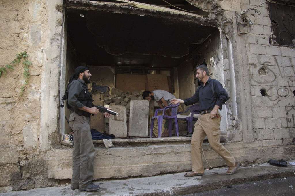 - Un rebelle s'amuse avec une arme en plastique. Derrière lui, un autre combattant prie dans une boutique en ruines. Deir al-Zor, le 13 juillet 2013.